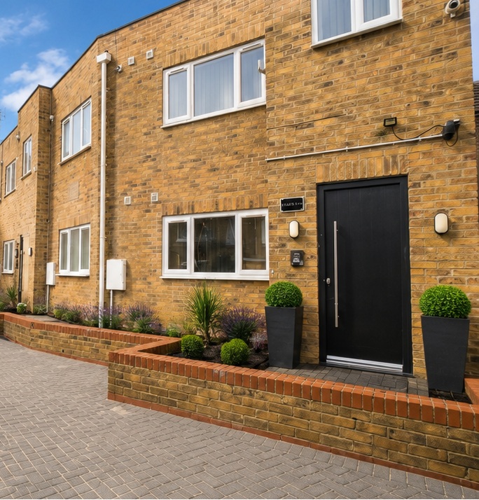 A well-maintained brick property with a black front door and planted front garden